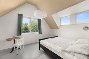 Un dormitorio con cama, ventana con cortinas, una mesita con silla y una lámpara en el techo.