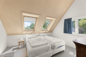 Un dormitorio con techo inclinado, dos tragaluces, una cama, una mesita de noche y un ventanal con cortinas.