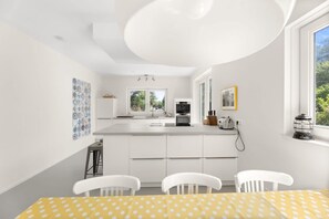 Una cocina moderna con armarios blancos, una isla central y una zona de comedor con una mesa amarilla y sillas blancas.
