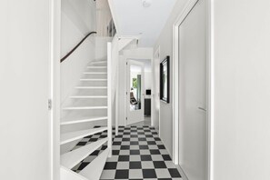 A hallway with a black and white checkered floor, white walls, and a white staircase.