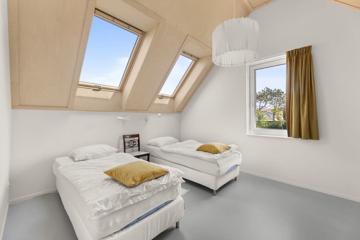 Ein Zimmer mit zwei Betten, einem Oberlicht, einer Hängelampe und einem mit Vorhängen versehenen Fenster.