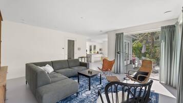 Een moderne woonkamer met een grijze modulaire bank, een klein bijzettafeltje, rieten stoelen en uitzicht op een balkon met tuinmeubilair.