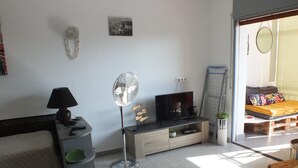 En moderne stue med en sofa, fjernsyn, en ventilator og et lille bord med en lampe.