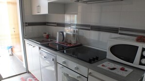Et moderne køkken med hvide hårde hvidevarer, opvaskemaskine, ovn, mikroovn og komfur.