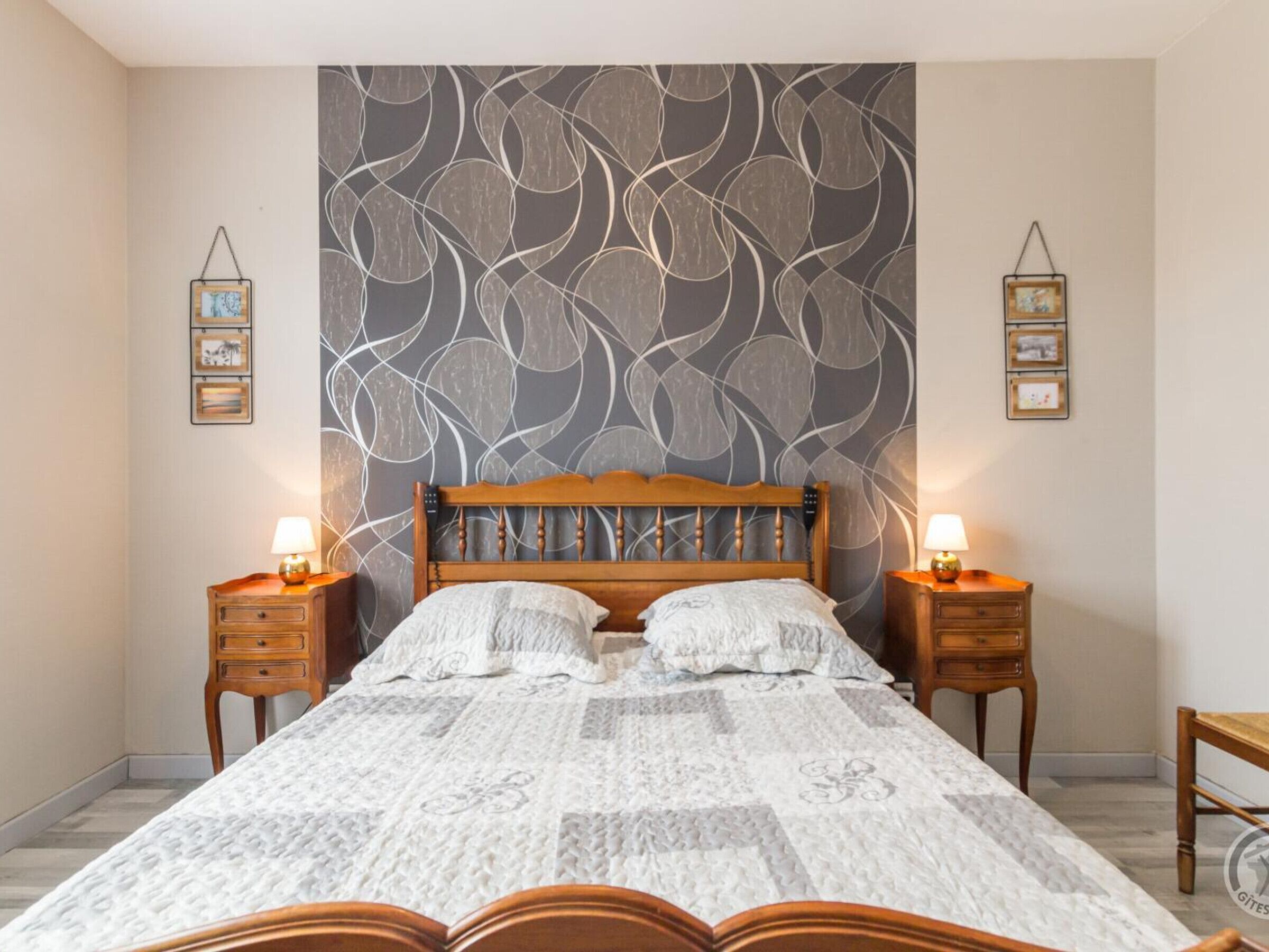 Quarto com cama grande, cabeceira de madeira, duas mesas de cabeceira com luminárias e papel de parede estampado.