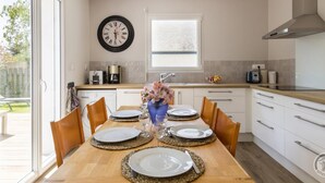 A modern kitchen with a dining table set for four, a clock on the wall, and a window providing natural light. - Contemporary 3-bedroom house near the beach in Saint-Pair-sur-Mer (Saint-Pair-sur-Mer)