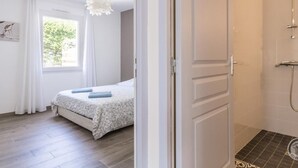 A bedroom with a bed, a window with curtains, a hanging light fixture, and a shower area with a tiled floor. - Contemporary 3-bedroom house near the beach in Saint-Pair-sur-Mer (Saint-Pair-sur-Mer)