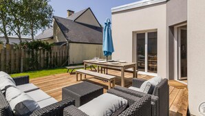 A patio with wicker furniture, a table set for dining, and a blue umbrella. - Contemporary 3-bedroom house near the beach in Saint-Pair-sur-Mer (Saint-Pair-sur-Mer)