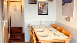 Un comedor con una mesa de madera dispuesta para seis personas, una lámpara colgante negra y cuernos de ciervo enmarcados en la pared.