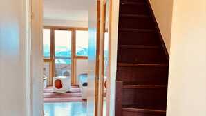 Un interior moderno con una escalera, una cama para mascotas y vistas a montañas a través de amplios ventanales.