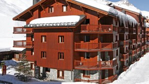 Un immeuble en bois à plusieurs étages, doté de balcons, se dressant sur fond de montagnes enneigées.