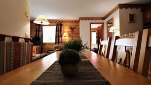 Une table à manger en bois, surmontée d’un set de table en fibres tressées, entourée de chaises à ossature en bois. Un pot de plante est placé au centre.