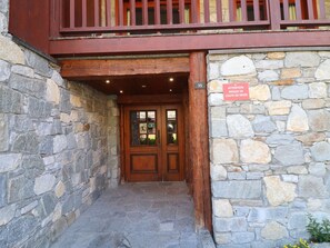 Enter a historic stone building with a balcony above and a wooden door.