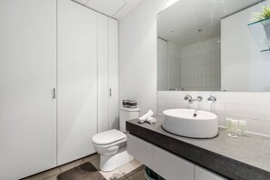 Bathroom features a white toilet, sink, and large mirror, along with a shelf for toiletries and a towel.