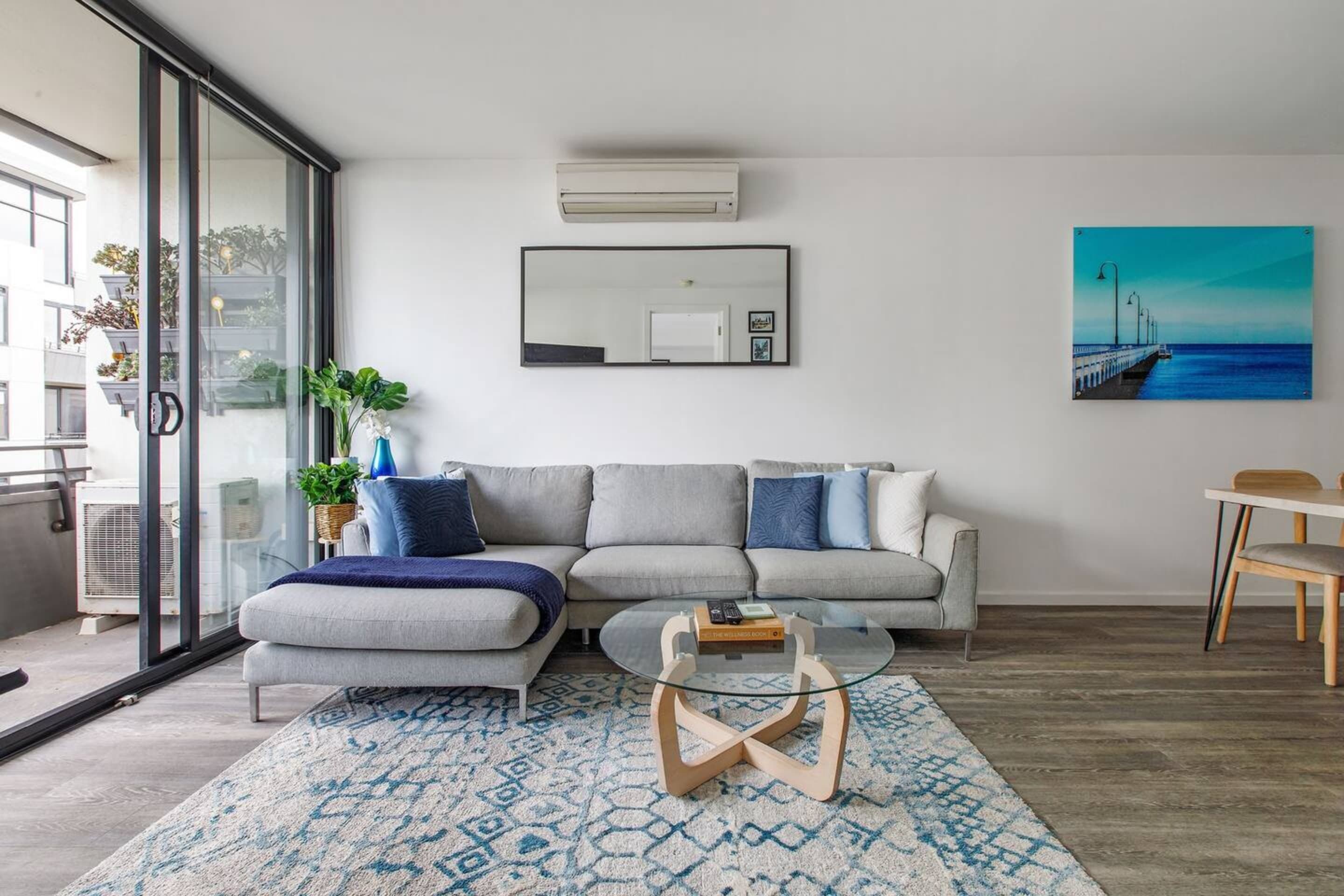 Ein modernes Wohnzimmer mit grauem Sofa, einem Glastisch und einem gemusterten Teppich.