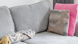 Un divano grigio con una coperta a motivi e un cuscino rosa.