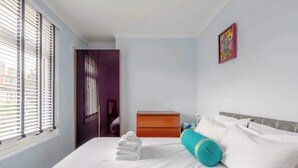 Una camera d'albergo con un letto, un comodino, una finestra con tende e una porta che dà su un'altra stanza.