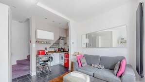 Un soggiorno moderno con un divano grigio, un tavolino in legno e un angolo cottura con un elettrodomestico rosso.