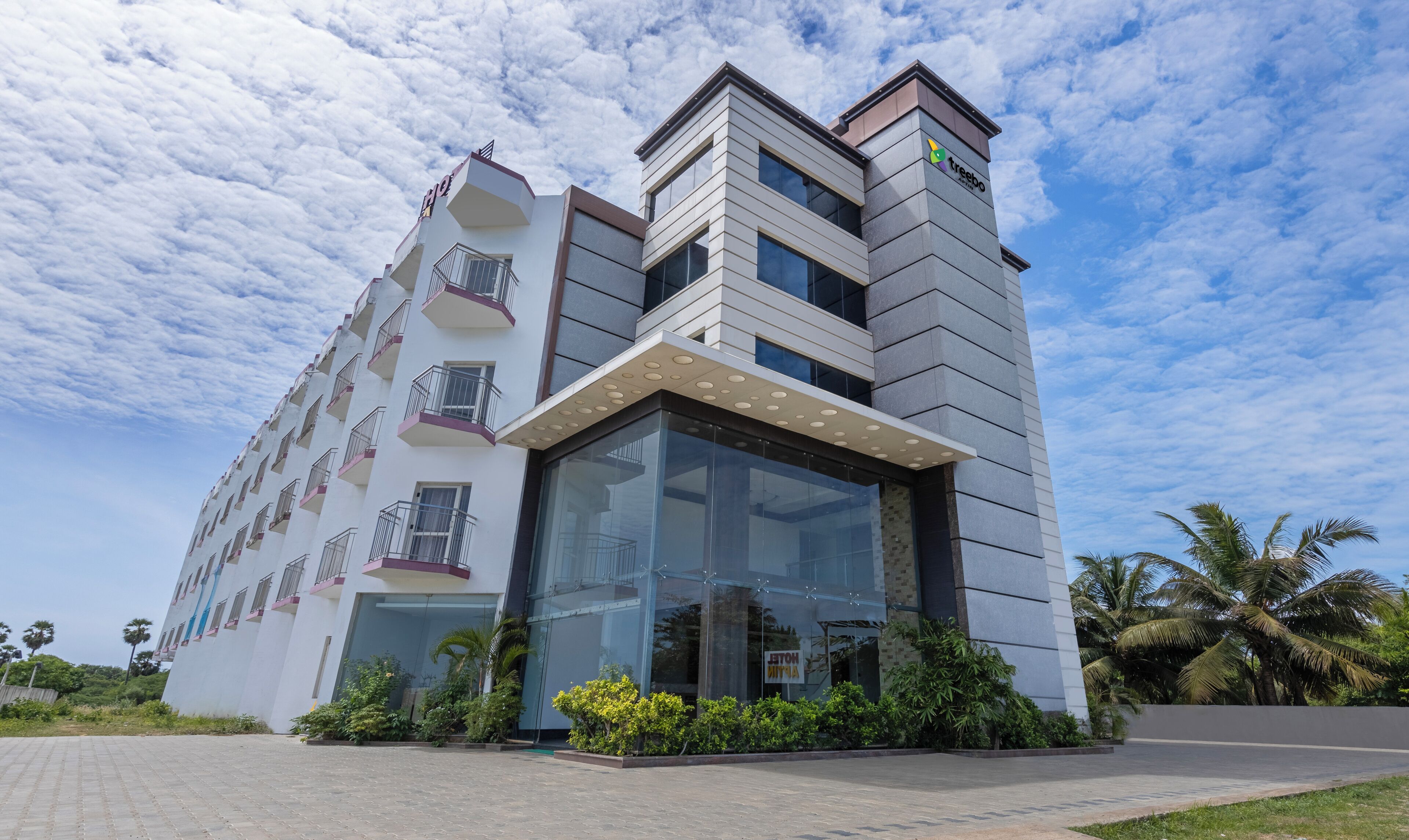 A modern hotel with a glass facade, multiple balconies, and a sign indicating it is a hotel.