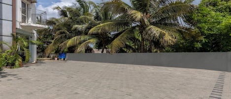 Un cortile pavimentato con palme, un muro grigio e un edificio con balconi.