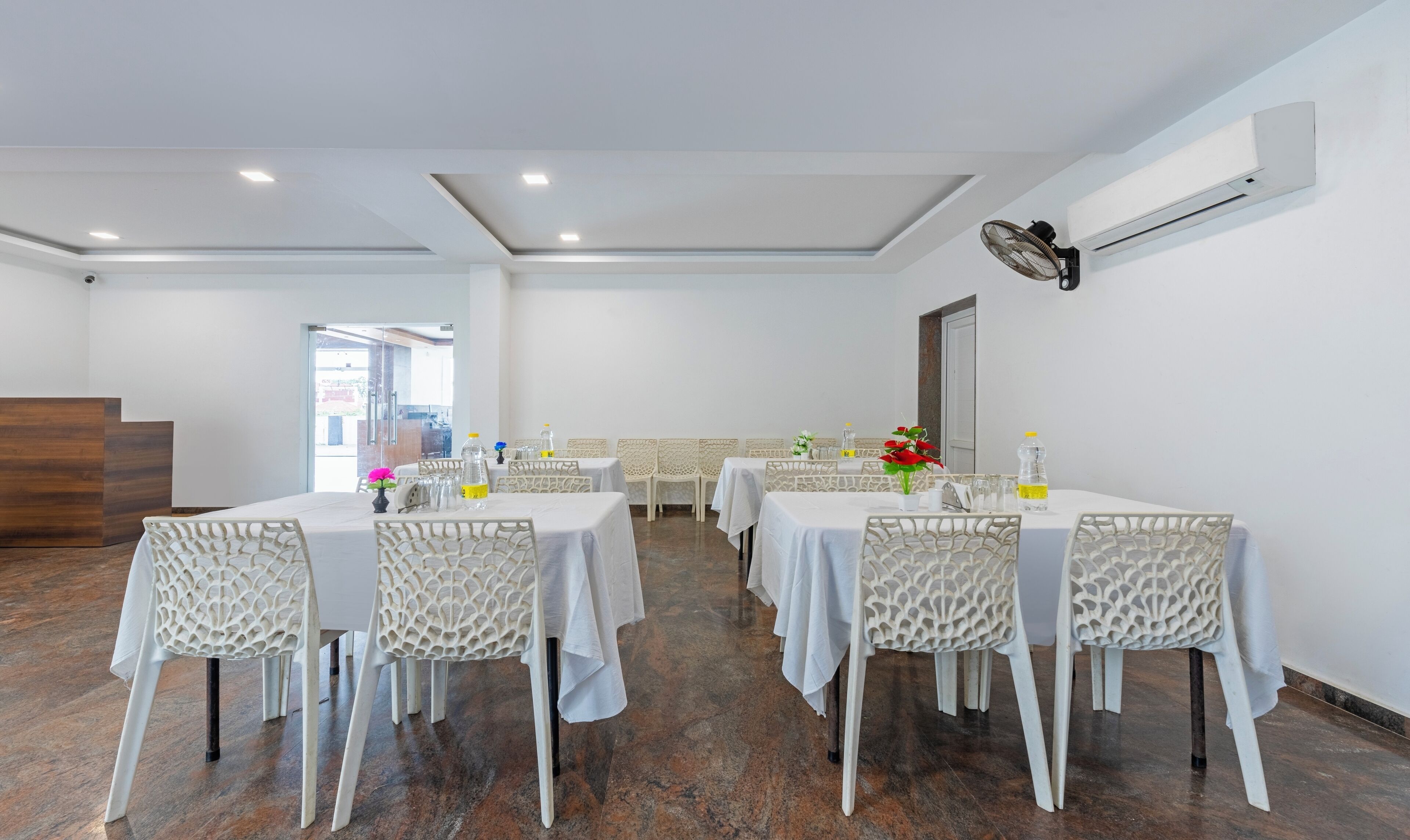 A conference room with white tables and chairs, a wooden reception desk, and an air conditioning unit on the wall.
