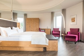 A modern hotel room with a wooden bed, a desk, a chair, and a large wardrobe.