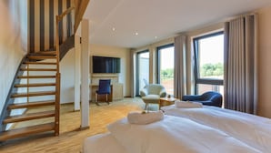 A hotel room with a wooden staircase, a bed with white linens, a desk with a chair, and large windows offering a view.