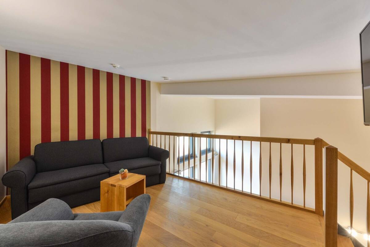 Ein Wohnzimmer mit einer schwarzen Couch, einem grauen Sessel und einem Holztisch.