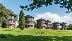 A row of brick apartment buildings with balconies, a grassy lawn, and trees. - Hotel & Golfrestaurant Gut Wissmannshof (Staufenberg)