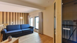 A living room with a blue sofa, wooden flooring, a wooden staircase, and a striped wall. - Hotel & Golfrestaurant Gut Wissmannshof (Staufenberg)