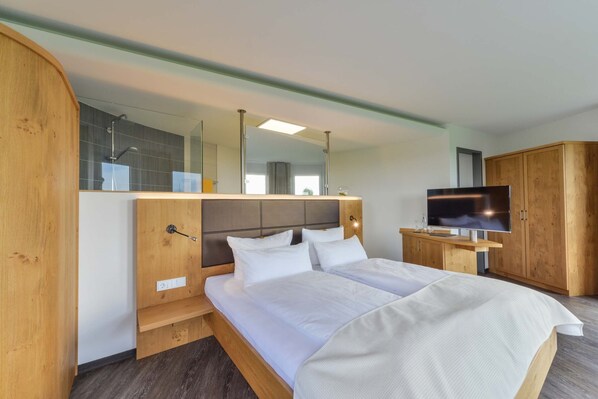 A hotel room with a large bed, wooden headboard, a television on a wooden stand, and a mirror above the bed.