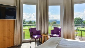 A hotel room with a large bed, two purple chairs, a small table, and a TV. - Hotel & Golfrestaurant Gut Wissmannshof (Staufenberg)