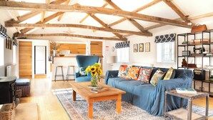 A spacious living room with a wooden ceiling, a blue sofa, a wooden coffee table, and a patterned rug. - The Coach House at Jervaulx (Ripon)