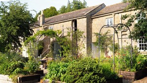 A stone building with a garden in front, wooden raised beds, and a metal trellis structure. - The Coach House at Jervaulx (Ripon)