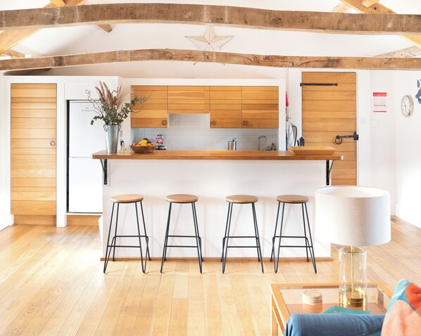 A modern kitchen with wooden cabinets, a central island with stools, and a dining area with a table and chairs.