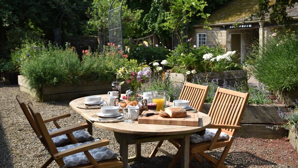 A round wooden table with chairs, set outdoors with a garden view. - The Coach House at Jervaulx (Ripon)
