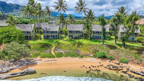 Ein Strandresort mit mehreren bungalowartigen Gebäuden, einem Sandstrand und einer felsigen Küstenlinie.