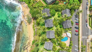 Eine Vogelperspektive zeigt ein Resort mit mehreren bungalowartigen Gebäuden, einem Strand und einem Schwimmbecken.