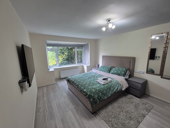 A bedroom with a bed, bedside table, and a window with a view of greenery.
