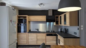 A modern kitchen with wooden cabinets, a black countertop, a built-in oven, and a dishwasher. - La Talonnière, Maison de Village Avec Terrasse (Messas)