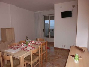 A dining area with a table set for four, a television mounted on the wall, and a view through a glass door.