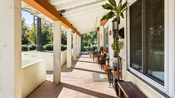 A covered patio area with a seating arrangement, a potted plant, and a view of the surrounding greenery. - Quiet Central Phx Home w/ enclosd yard, jungle gym (Phoenix)