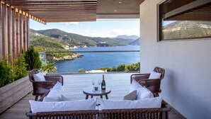 Un balcon agrémenté de meubles en osier, une table avec une bouteille et des verres, et une vue sur un lac et des montagnes.