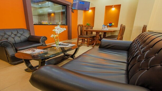 Un salón con una mesa de centro de vidrio, dos sofás de cuero negro, una mesa de comedor con sillas y un televisor montado en la pared.