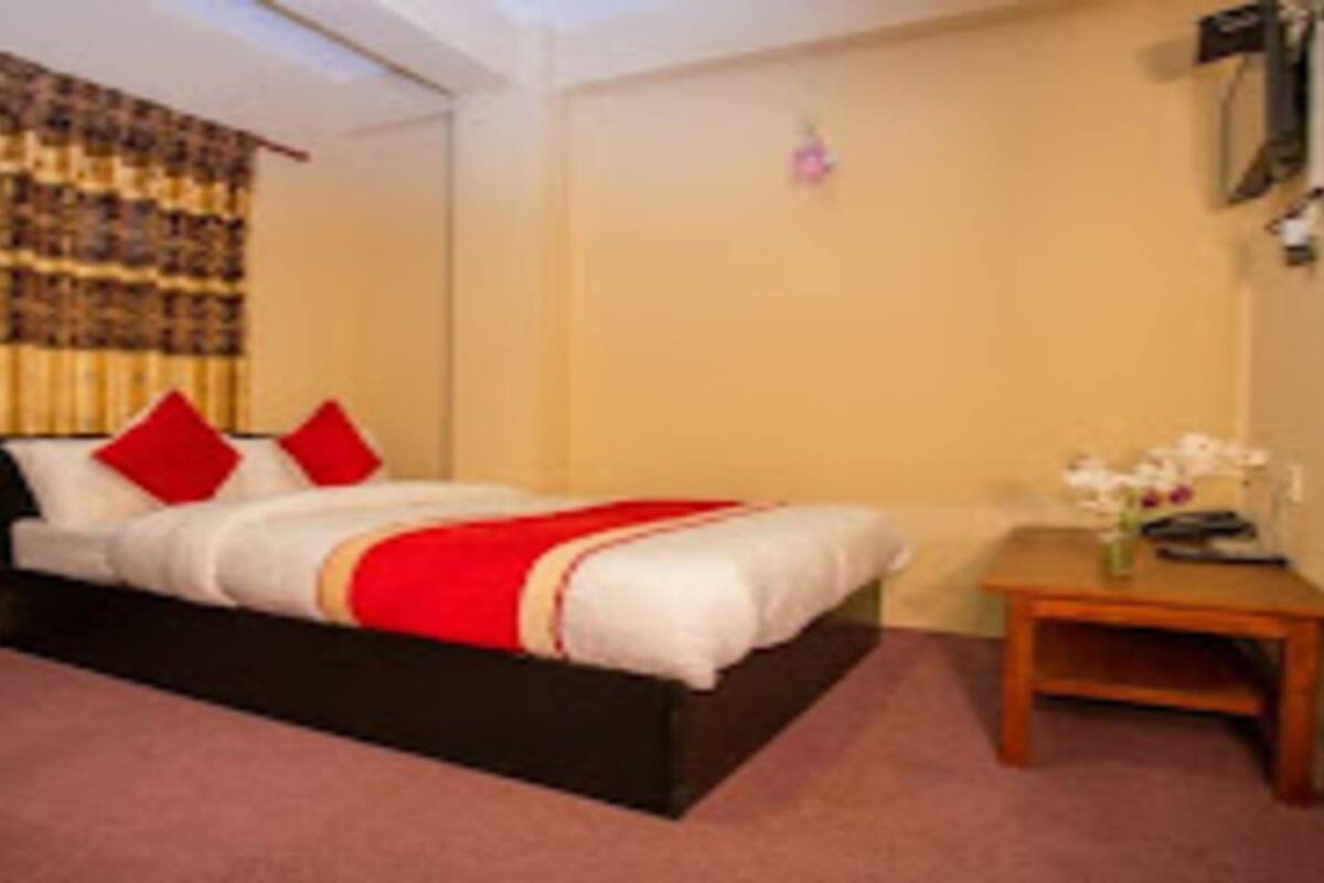 A bedroom with a bed, a nightstand, a small table with flowers, and a curtain.