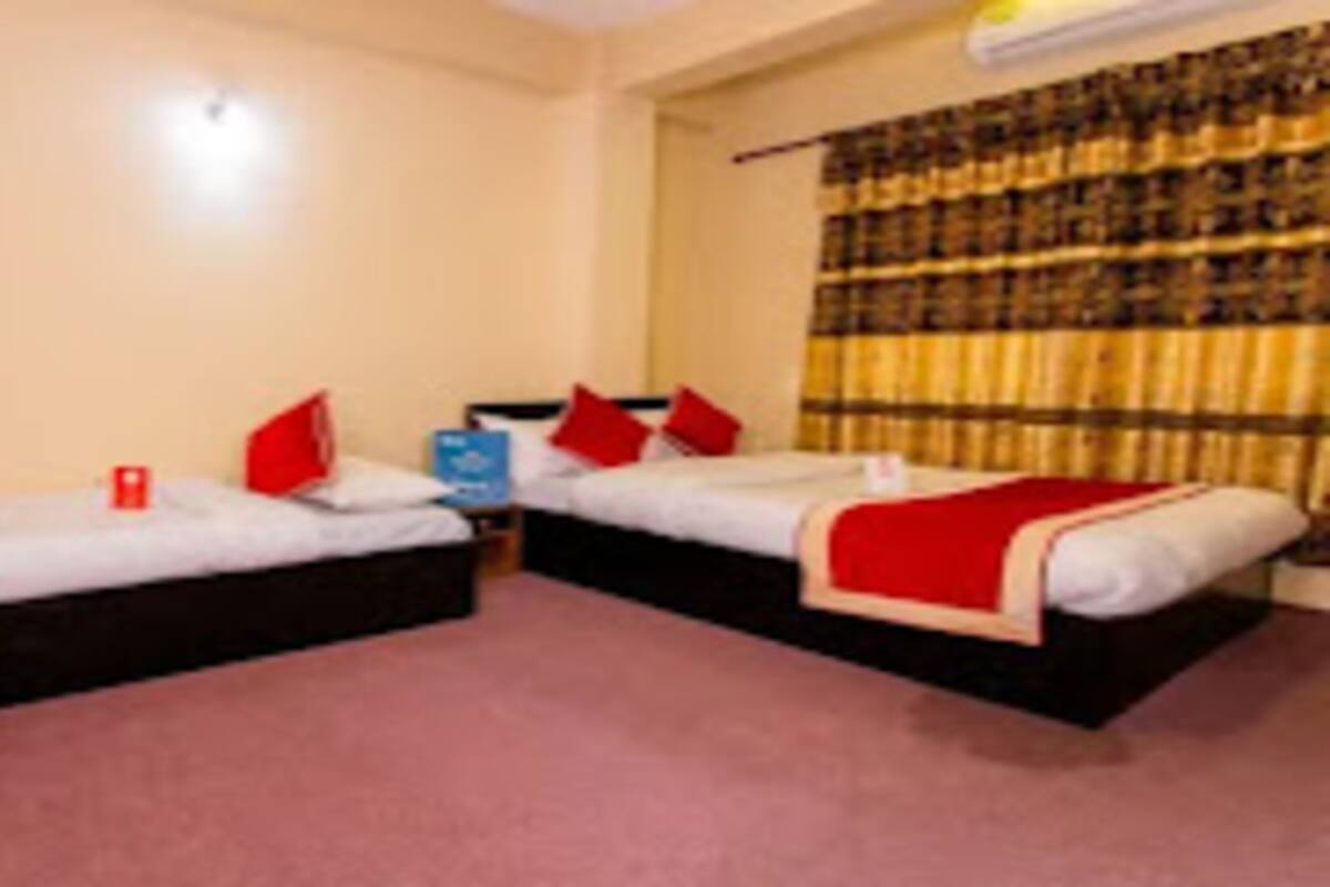 A room with two beds, each with a red blanket and pillows, a small table, and a curtain with a plaid pattern.