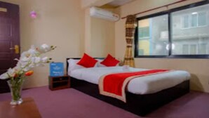 Habitación de hotel con cama, mesita de noche, un jarrón con flores y ventana con cortinas.