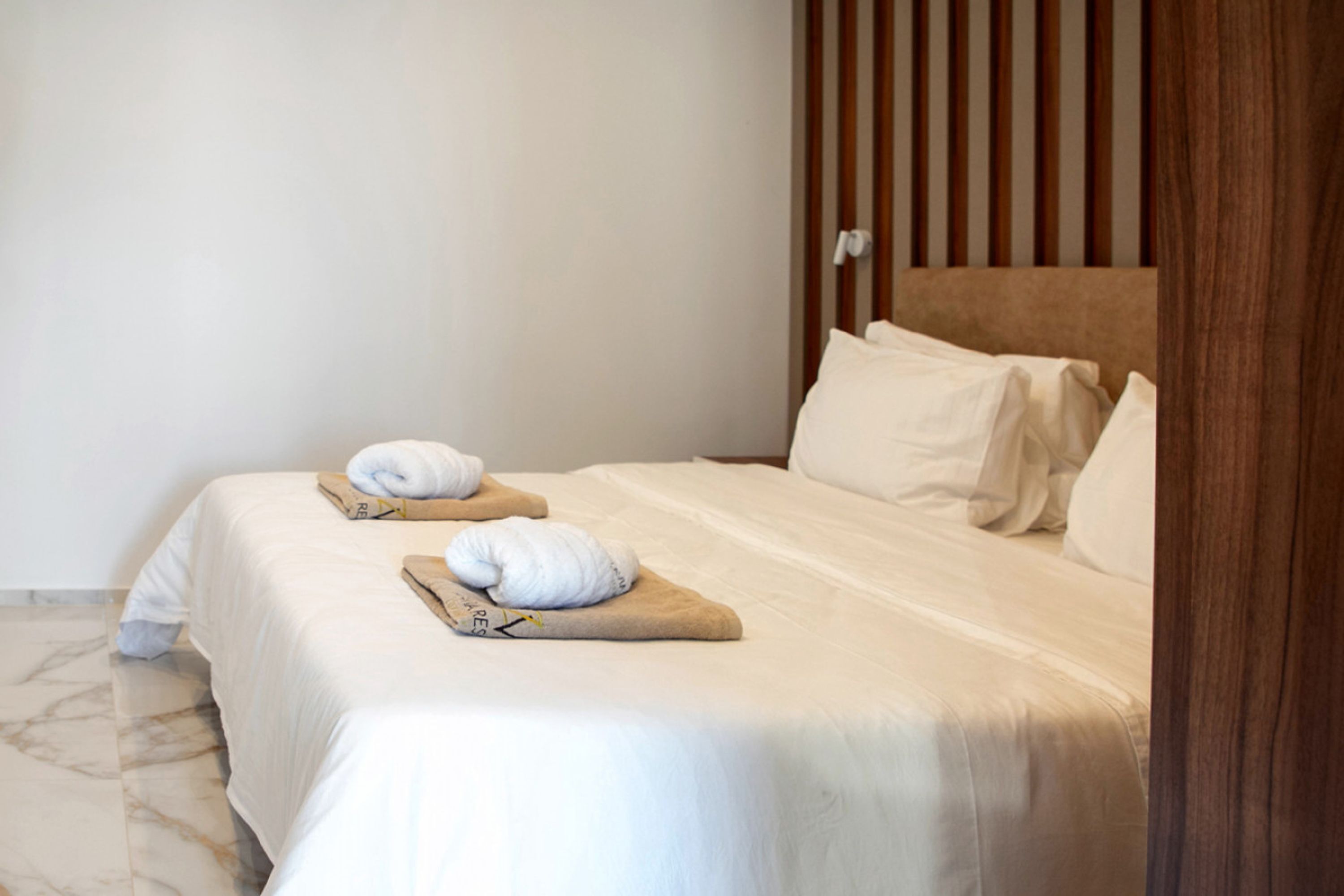 A neatly made bed with white linens and two towels on a wooden tray.