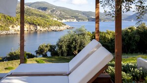 A lounge chair with a white cushion, positioned under a wooden pergola with a view of a lake and surrounding greenery. - Zavia Alpha in Syvota (Igoumenitsa)