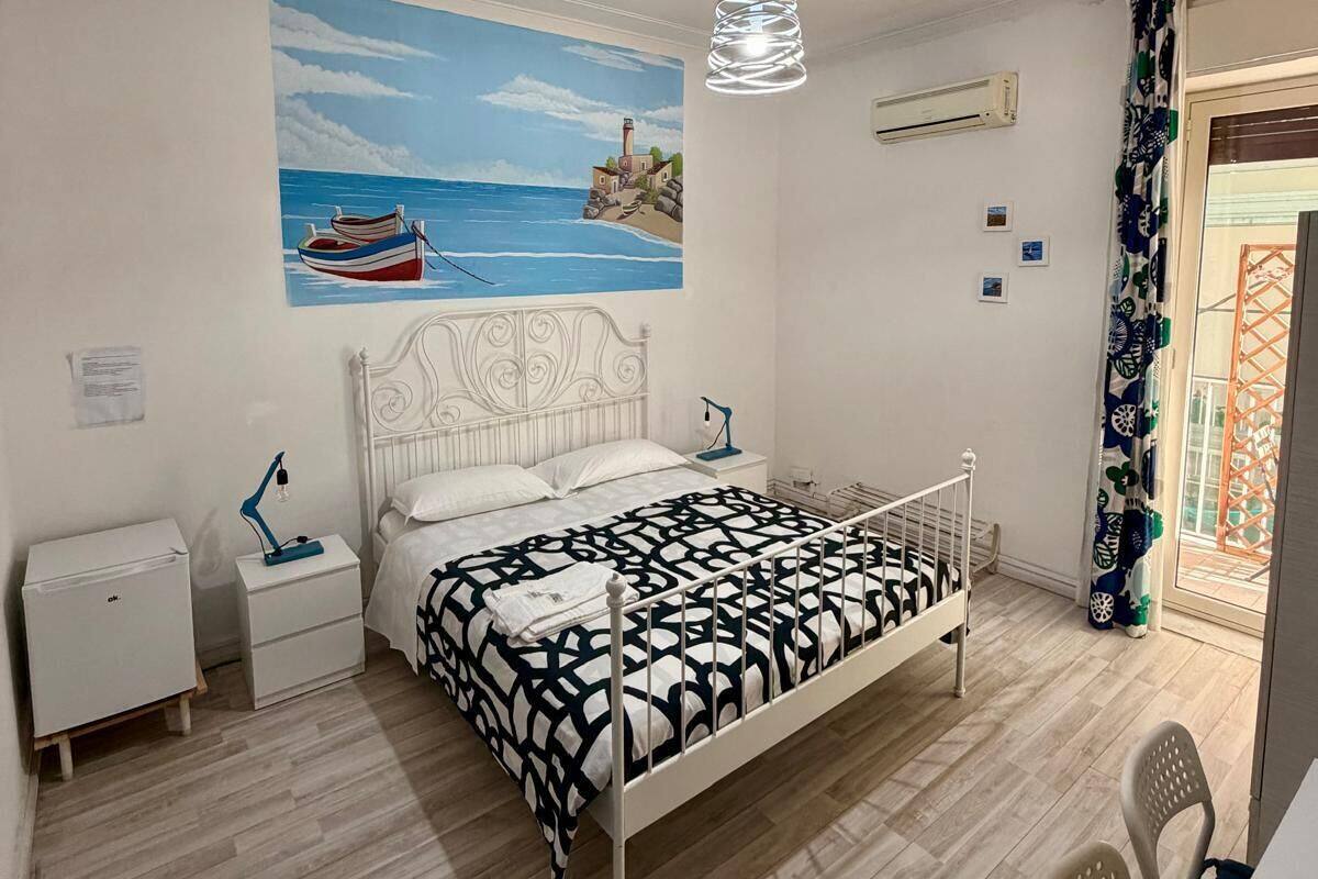 Une chambre à coucher comprenant un lit, une table de chevet, un bureau, une chaise, un tableau et une fenêtre avec des rideaux.